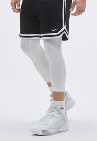 Μαύρα αθλητικά σορτς με λευκές ρίγες, συνδυασμένα με λευκά συμπιεστικά κολάν και γκρι αθλητικά παπούτσια με κόκκινο λογότυπο.