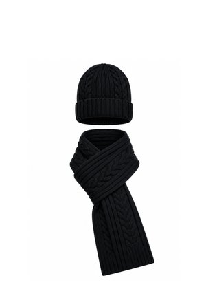 Bonnet en laine noire tricotée et écharpe épaisse assortie avec des motifs torsadés et côtelés sur fond blanc.