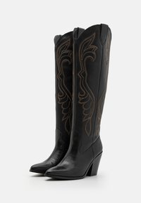 Botas de vaquero de cuero negro con punteras puntiagudas y un tacón de 3 pulgadas. Diseños bordados marrones intrincados adornan el caña. Acabado texturizado en las puntas.