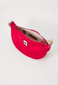 Borsa in nylon rosso con forma curva e una tracolla di un beige chiaro. Presenta una chiusura con zip e un'icona giocosa con occhiali da sole sulla parte frontale.