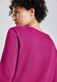 Magenta Pullover mit einem lässigen Rundhalsausschnitt und langen Ärmeln, aus einem weichen, strukturierten Stoff gefertigt. Der Fokus liegt auf der Rückansicht und der Kurvatur.