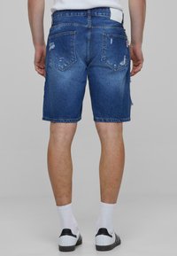 Donkerblauwe denimshorts met ver distressed details, een gerafeld zomen en vijf zakken. Draagt met witte sokken en zwart-witte schoenen.