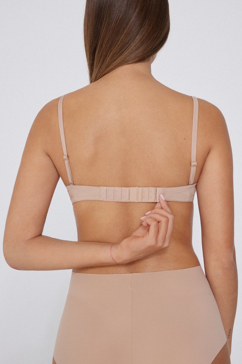 Sujeción nude vista desde la parte posterior, con tirantes ajustables, un cierre de gancho y ojal, y una textura de tela suave.