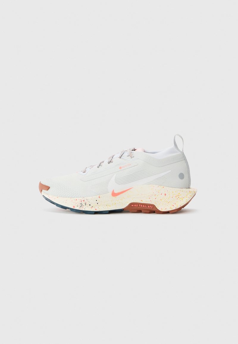 Chaussure de trail running Nike blanche et gris clair avec une semelle intermédiaire crème mouchetée, des accents corail et une semelle extérieure en caoutchouc, vue de profil sur fond blanc.