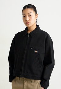 Zwarte ritsjack van katoen, met een kraag, zijzakken en een voorzak met logo-detail. Losse pasvorm.