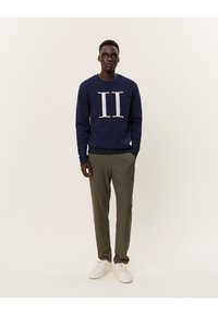 Sudadera marina con gráfico blanco "II", mangas largas y escote redondeado. Combinada con pantalones verde oliva y zapatillas blancas. Diseño sencillo.