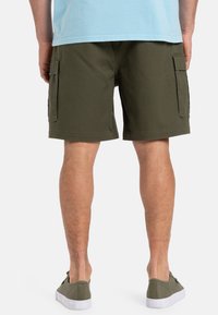 Olivenfargede cargo-shorts med to sidelommer, laget av bomull. Brukt med grå fottøy. Bakvisning viser en avslappet passform og hemlengde.