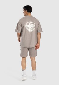 Grå bomulds t-shirt og shorts sæt med et hvidt grafisk logo på ryggen. Løs pasform med korte ærmer og elastisk talje.