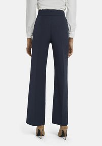 Marineblauwe wijde broek met een hoge tailleband, een gladde textuur en een geplooid voorpand, gecombineerd met beige hoge hakken.