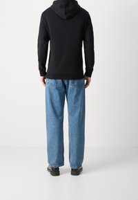 Czarny hoodie z długimi rękawami, noszony z jasnoniebieskimi spodniami dżinsowymi o luźnym kroju i czarnym obuwiem, widziany z tyłu.