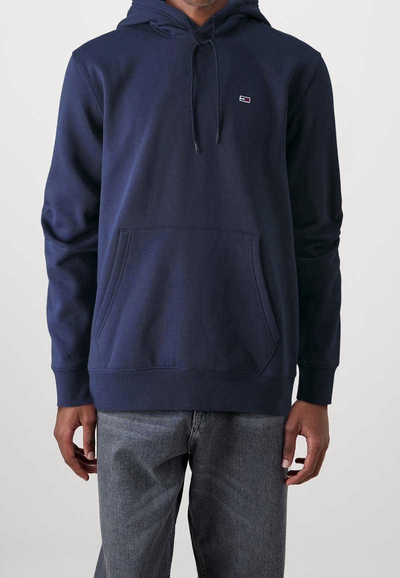 Sudadera azul marino hecha de una mezcla de algodón, con un bolsillo tipo canguro, capucha con cordón y un pequeño logo en el pecho. Textura suave.