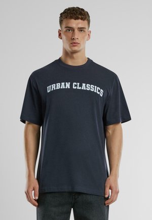 T-shirt en coton bleu marine avec une coupe oversize, col rond, et "URBAN CLASSICS" imprimé en blanc contrasté sur la poitrine.