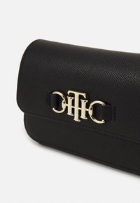 Borsa a tracolla in pelle nera con texture, dotata di un pattina curvata e accessori in metallo dorato con logo. Design compatto e rettangolare con una finitura liscia.