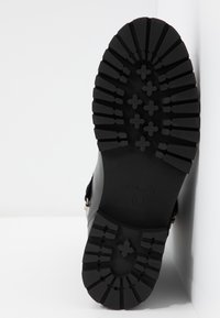 Semelle de botte en caoutchouc noir avec des motifs saillants, surface texturée, logo gravé, et détails de taille. Présente un design robuste pour une utilisation en extérieur.