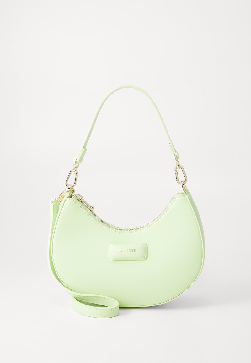 Bolsa de mão em imitação de pele verde com formato de crescente, hardware em tom dourado, fecho em zíper e alça de ombro destacável. Logótipo da Lacoste exibido.