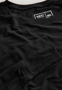 Chemise noire à manches longues en tissu doux ; dotée d'un col rond et de détails cousus sur les manches et les côtés.