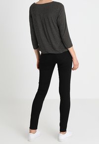 Schwarz-weiße gemusterte Bluse mit lockerer Passform und Dreiviertelärmeln, kombiniert mit engen schwarzen Jeans und weißen Sneakers.
