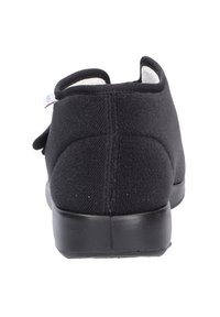 Schwarzfarbener Schuh aus einem weichen Stoff mit runder Form und niedrigem schwarzem Gummi-Sohle. Verfügt über einen Klettverschluss zur Schließung.