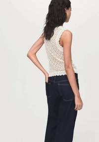 Krämfärgad virkade topp med vågiga kanter, ihopparad med mörkblå vida jeans. Toppen har en delikat, öppen stickad design.