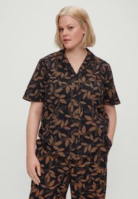 Camisa negra de manga corta con un patrón de hojas beige en toda la prenda, con cuello de solapa y cierre de botones, hecha de tela ligera.