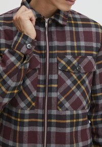 Geruite zip-up jas in bordeaux, grijs en zwart met gele accenten; beschikt over twee borstzakken en een gestructureerde stofafwerking.