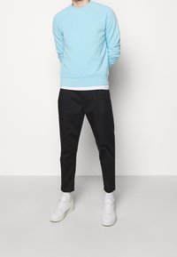 Sudadera azul claro con cuello redondo y puños acanalados, combinada con pantalones negros a medida y zapatillas blancas. Textura suave, ajuste informal.