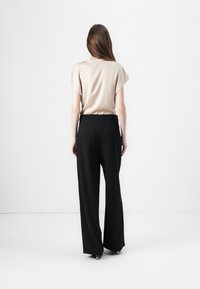 Beige kortermet topp og svarte vide bukser, vist fra baksiden. Glatt stoff med en avslappet passform, minimalistisk design.