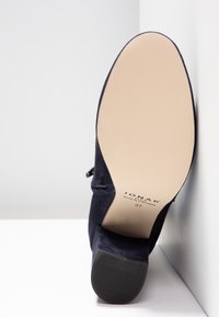 Chaussure à talon haut en daim bleu marine avec un bout arrondi et lisse et une semelle en caoutchouc texturée. L'extérieur présente un détail de couture subtil. Taille 37.