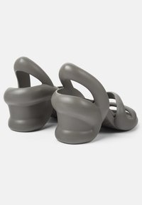 Sandali grigi stampati con un design ondulato, apertura sul retro e un tacco curvo distintivo, caratterizzati da una texture liscia e cinturini con fori.
