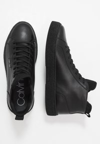 Černé kožené vysoké tenisky s texturovanou černou gumovou podrážkou, šněrováním v přední části a poutkem na patě. Viditelné logo "Calvin Klein".