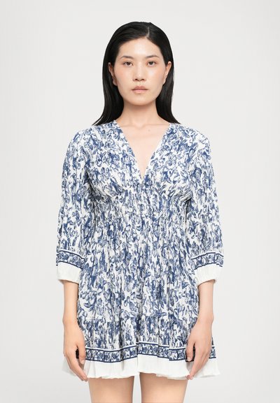 Robe à motif floral bleu et blanc avec manches longues, encolure en V, taille froncée et détails en volant au bas. Tissu léger.