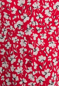 Punainen kangas, jossa on valkoisia ja mustia kukkakuoseja, ja keskellä on pystysuora rivi punaisia nappeja.