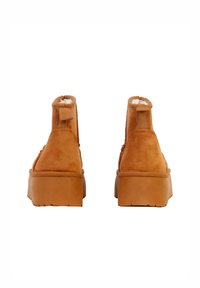 Ruskind ankelstøvler i tan med en tyk sål, der har en bageste trækflap og blødt for synligt ved den øverste kant. Glat tekstur og afrundet form.