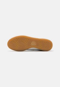Shoe outsole featuring a gum rubber sole with a textured pattern and embossed letters. Color is light brown with yellow undertones.