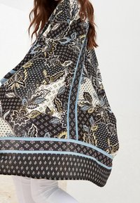 Écharpe noire et crème à motifs floraux et géométriques, rehaussée d'une bordure bleue et d'une texture agréable au toucher.