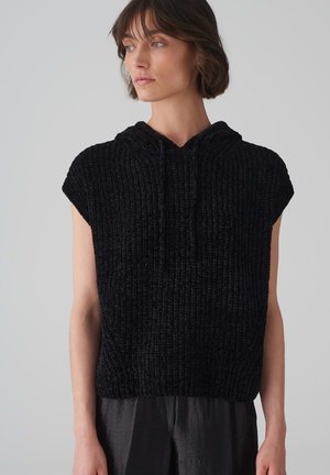 Black knitted hoodie tank top with cap sleeves, featuring a textured pattern and drawstring hood. Worn with dark, flowy pants.