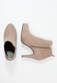 Beige semišové kotníkové boty s špičatou špičkou, úzkým vysokým podpatkem a bočním zipovým detail. Hladká textura s minimem prošívání.