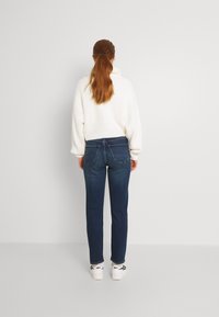 Dark blue jeans with a slim fit and back pockets, paired with a chunky white sweater. White sneakers with black laces visible below.