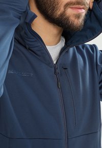 Marineblå hættejakke med en glat tekstur, der har en fuldlængde lynlås, sidelommer og "Mammut" logoet præget på brystet.