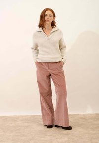 Maglione lavorato a maglia grigio chiaro con colletto zip e maniche larghe, abbinato a pantaloni a gamba larga in corduroy rosa. Scarpe con zeppa nere.