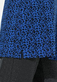Top in stampa leopardata blu con orlo arrotondato, caratterizzato da macchie nere su un tessuto morbido; abbinato a pantaloni neri con texture.