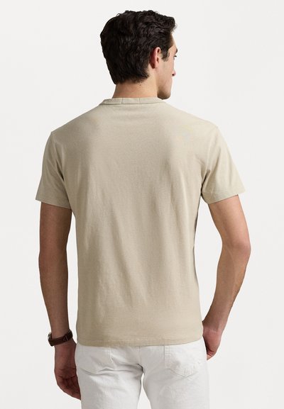 Beige t-shirt med kort ärm, rundad hals, mjukt tyg, slät textur, enfaldig design utan synliga mönster eller grafik, bärs med ljusa shorts.