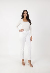 Top crema de cuello cuadrado y manga larga combinado con jeans blancos de tiro alto y sandalias de tacón de bloque transparentes. Texturas suaves y diseño ajustado.