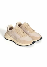 Zapatillas deportivas beige con parte superior de ante texturizado y sintético liso, que cuentan con una suela acolchada, diseño con cordones y suela exterior de goma negra.