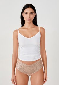 Camisola bianca in cotone con spalline sottili abbinata a perizoma beige in pizzo con motivi floreali e bordi ondulati.