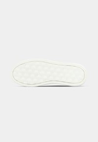 Witte rubberen zool van de schoen met een textuurpatroon voor grip en verhoogde logo's. Afgeronde randen en een dikke, geribbelde rand verhogen de duurzaamheid.