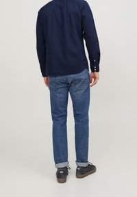Maglietta a maniche lunghe blu navy abbinata a jeans blu. I jeans sono leggermente svasati con risvolti. L'outfit è completato da sneakers nere casual.
