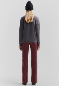 Grijze longsleeve top met een ontspannen pasvorm, gecombineerd met aansluitende bordeauxkleurige neplederen broek; model draagt een zwarte gebreide beanie. Achteraanzicht.