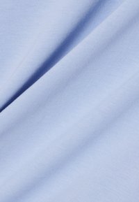 Tissu en coton bleu clair avec une texture lisse, présentant de légères côtes diagonales et des plis doux qui tombent délicatement.