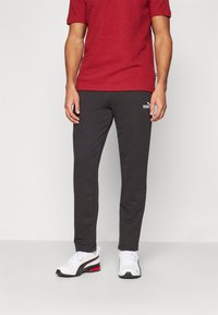 Mørkegrå joggebukser med elastisk midje, med en liten hvit Puma-logo. Kombinert med en rød teksturert skjorte og hvite treningssko.